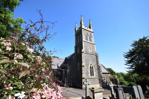 A photograph of Glengormley Carnmoney Parish Church, pictured behind a flowering bush.