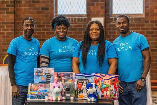 Four people stand inside RCCG Church in Edinburgh, with a table of gifts in front of them