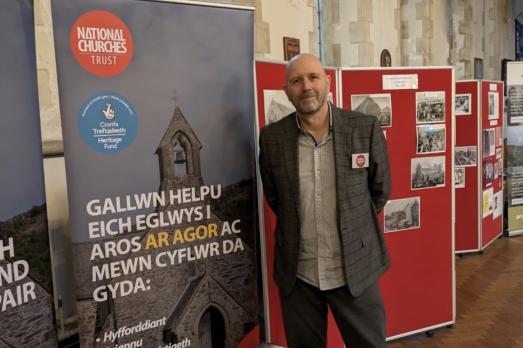 A man in a suit stands next to a pull up banner that in in Welsh