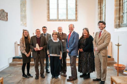 eight people stand together. National Churches staff and Chair with the team at St James the Great who are holding their 'Church of the Year' trophy. Everyone is smiling.