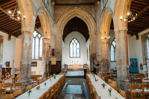 The interior of St James the Great with long tables in the aisle for people to sit at.