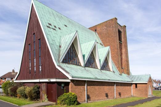 The exterior of Fleetwood St Nicholas church; a bold red brick building with a green roof.