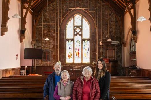 Four of the trustees of Tundergarth church inside the building. You can see stained glass in the background and pews on either side of the aisle.
