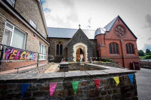 The outside of St Illtyd church with colourful flags and a banner saying 'welcome'.
