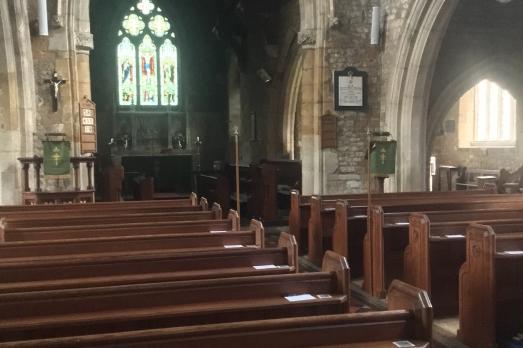 Rows of wooden pews facing a stoned archway, with the altar inside. A stained glass window is visible through the archway.