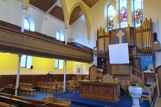 The inside of Selkirk and Ashkirk Parish church, with rows of wooden pews, a gallery, a font and an organ present.