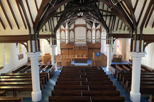 An interior shot of Bridge of Allan Parish Church. You can see a beam ceiling, rows of pews and columns. The pews are facing an organ.