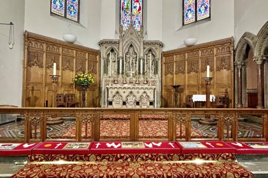 Facing the altar at Inverness Cathedral; red patterned carpet and colourful stained glass windows dominate the photo.