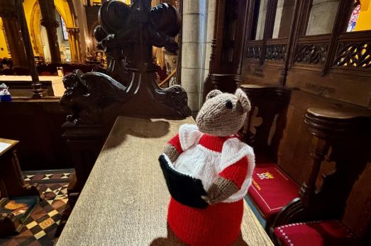 A knitted/crocheted mouse reading a Bible/Hymn book on a pew. This is part of a trail of church mice in the cathedral. 