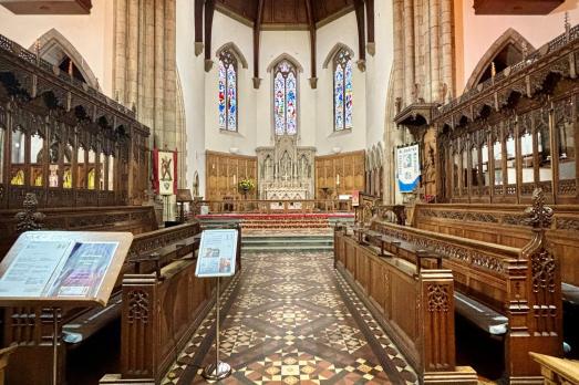 A patterned tiled floor with rows of pews either side and facing the altar; the is part of the interior of Inverness Cathedral