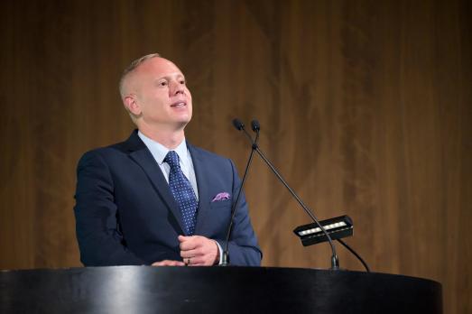 Rob Rinder in a suit stands at a podium