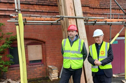 Two workers stood next scaffolding outside a red brick church