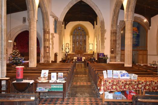 Impressive interior of the church with pews facing the altar with a large stained glass window behind. There are also many stone arches.