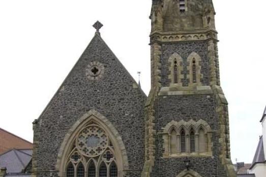 A large Victorian church with a tower to the right-hand side where the entrance to the church also is. Photographed on a busy street.
