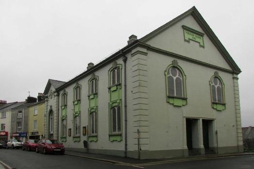 The end of a row of buildings sits the off-white colour Cornerstone church with beautiful windows.