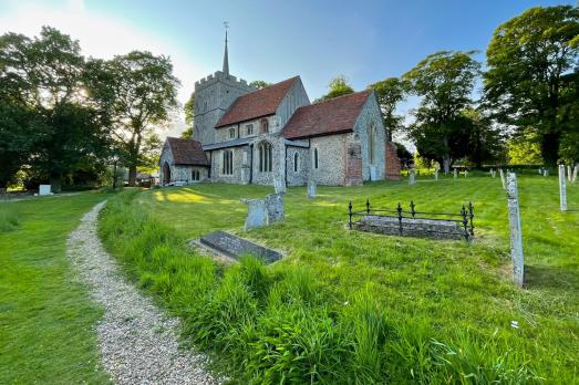 A path winds through a grassy graveyard up to a beautiful 1000+ year-old stone church with a red roof and tower.