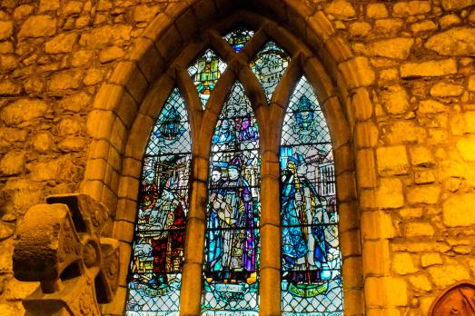 A colourful arched stained glass window surrounded by stone