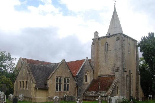 A large stone church with a red roof and prominent square tower on the left-hand side of the image. Photographed on a cloudy yet sunny day. 