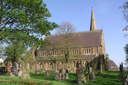 A beautiful stone church with many windows and a spire. There are some trees in the foreground.