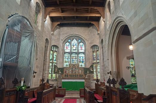The stone interior facing the altar. There are pews either side facing each other. An organ is  covered up.