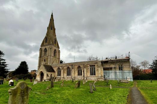 A beautiful stone church, St Peter Ad Vincula, photographed on a rainy day with men working on replacing the roof.