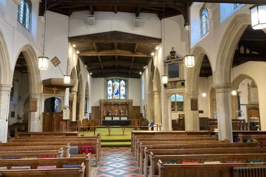 Stunning interior of St Mary; rows of wooden pews face an altar. There are stone arches either side.