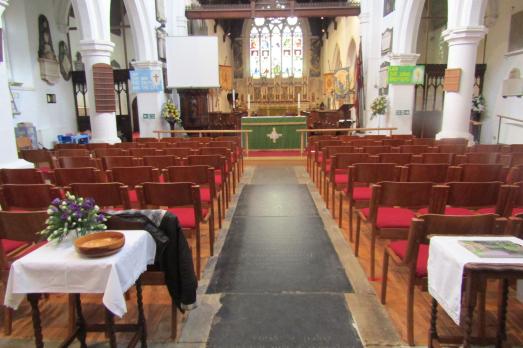 Interior of St Mary Magdalene; rows of red chairs face the altar, which has a large arched stained glass window.
