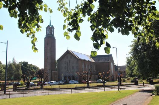 A striking church building with a prominent tower on the left-hand side of the building. There are trees and foliage in the foreground.