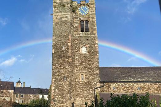 A stone church tower at Conwy St Mary with a rainbow behind it