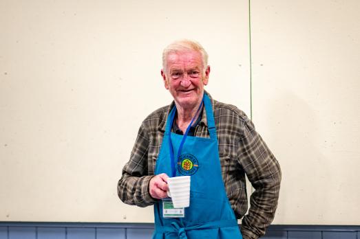 A man wearing an apron, holding a cup of tea