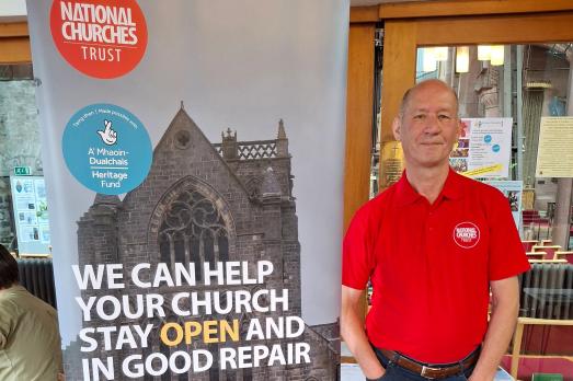 National Churches Trust Scotland Support Officer stands next to a pull up banner advertising what support we can provide to churches 
