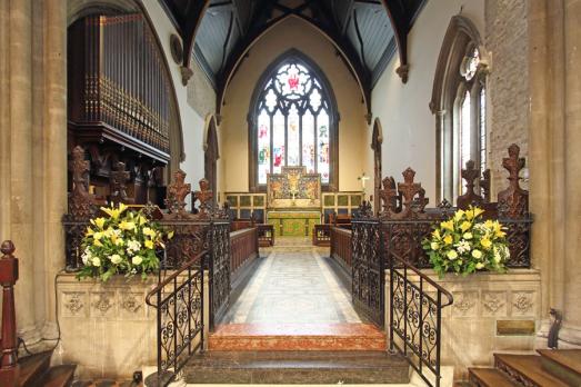 The interior of Christ Church with vases of yellow flowers present and a beautiful arched stained glass window