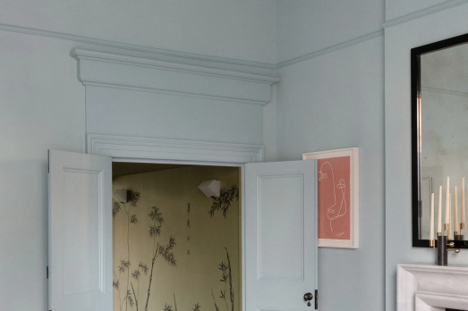 The image shows a room with pale blue walls, the doors are opeing into a yellow wallpapered room. 