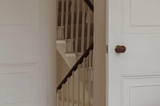 The image shows two white panneled doors opening to a white wooden staircase.