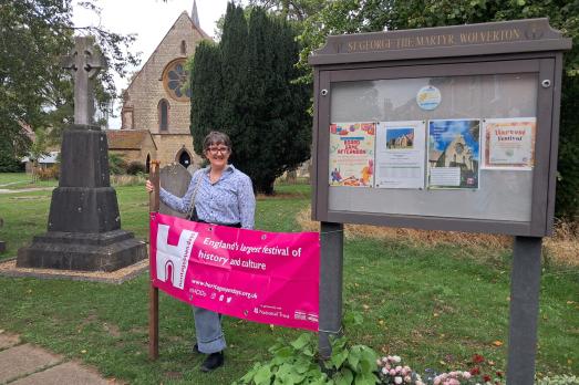 A woman stands next to a pink banner advertising a heritage day outside a church