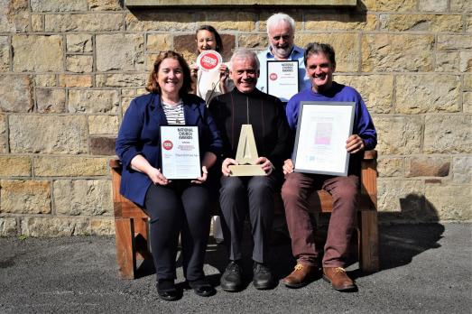 A group of five people sitting down and facing the camera while holiding awards and certificates