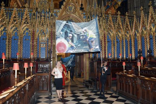 Two women hold a banner with the National Churches Trust logo on it in while walking down an aisle with pews either side