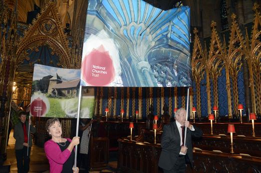 A man and a woman holding a banner with the National Churches Trust logo on inside Westminster Abbey