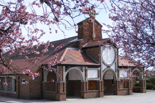 A church building with arched details on the front and blossom trees surrounding the building