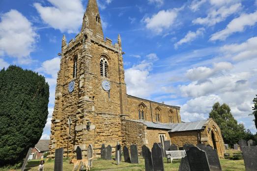 A beautiful warm stone church with a prominent tower and spire