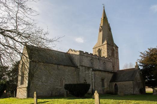 A stone church with a tower and spire to the right of the image