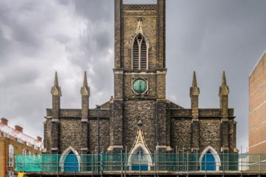 A large Gothic stone church with a tower in the centre. Scaffolding envelopes the bottom of the building and graffiti is visible 