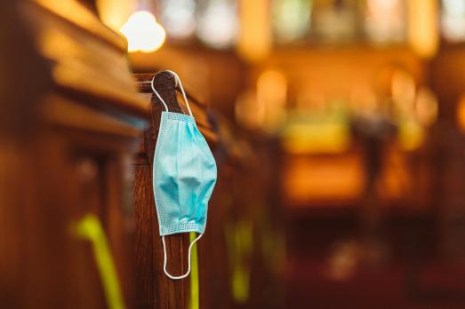 A facemask hanging from the side of a wooden pew