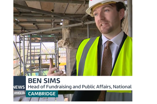 A screenshot of Ben Sims, wearing a high vis jacket and a hardhat, being interviewed on the scaffolding of a church making repairs.