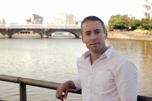 A man leans against a railing with a river behind him