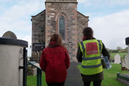 Two women, one wearing a high vis, walk up to an old church building
