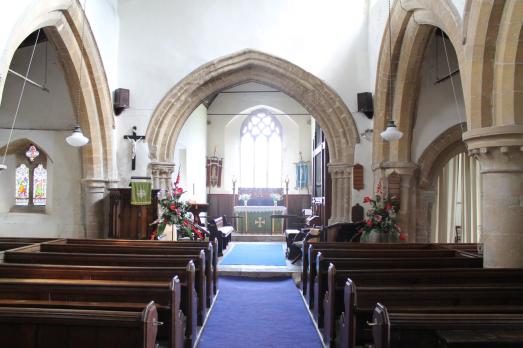 The interior of St James; rows of wooden pews faced an archway and altar.