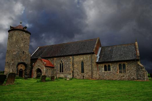 A round tower grey stone church pictured on a very stormy day