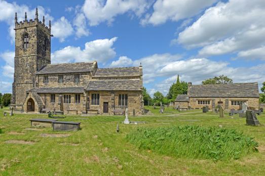 A large stone church with a tower on the left-hand side with lots of lush green grass in the foreground and a bright blue sky
