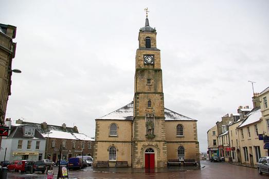 Exterior shot of a pale-coloured brick church with a tower, on a street with terraced buildings.